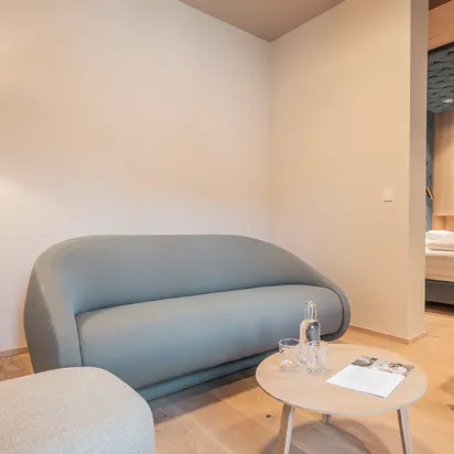 Modern hotel suite with wooden furniture, light blue sofa, and view into bedroom